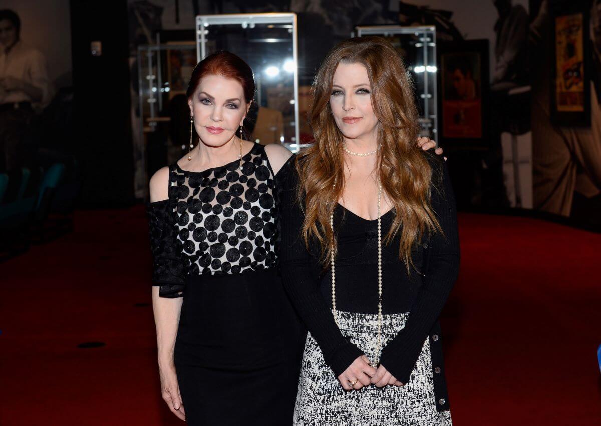 Priscilla Presley stands with her arm around Lisa Marie Presley's shoulders. They both wear black.