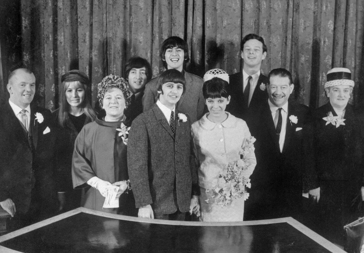 A black and white picture of Ringo Starr and Maureen Starkey on their wedding day. Maureen's father, Cynthia Lennon, Maureen's mother, John Lennon, George Harrison, Brian Epstein, and Ringo's parents surround them.