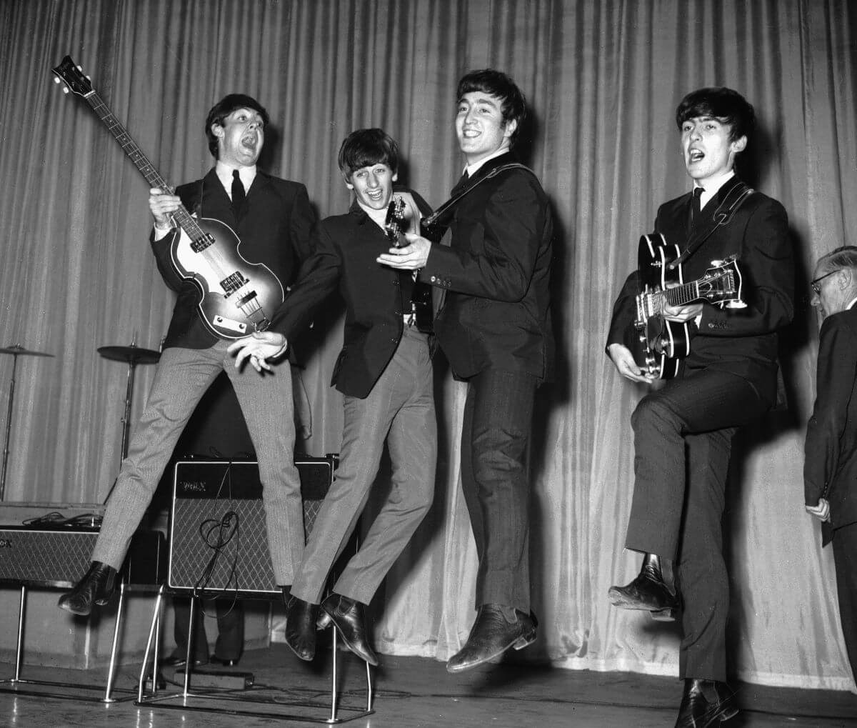 A black and white picture of The Beatles jumping into the air while on a stage.