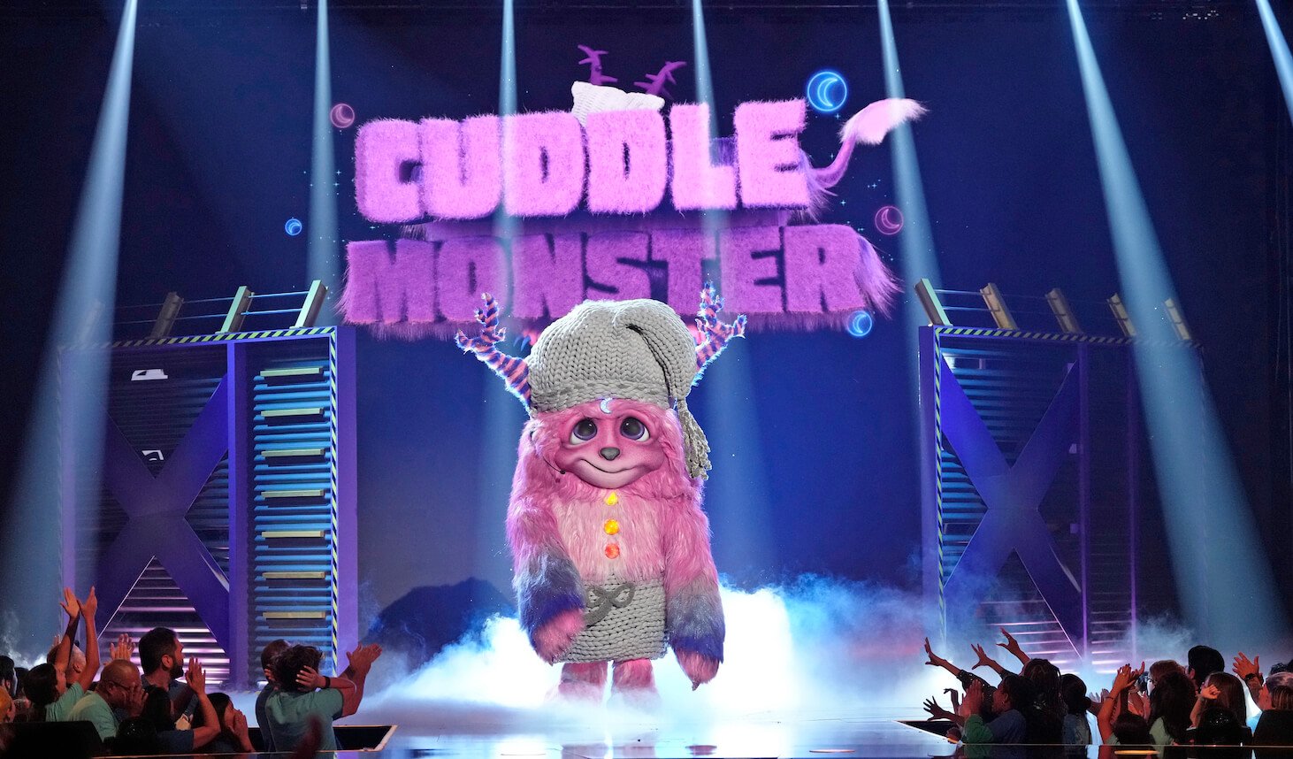 Cuddle Monster on stage in 'The Masked Singer' Season 10 with a 'Cuddle Monster' sign behind him