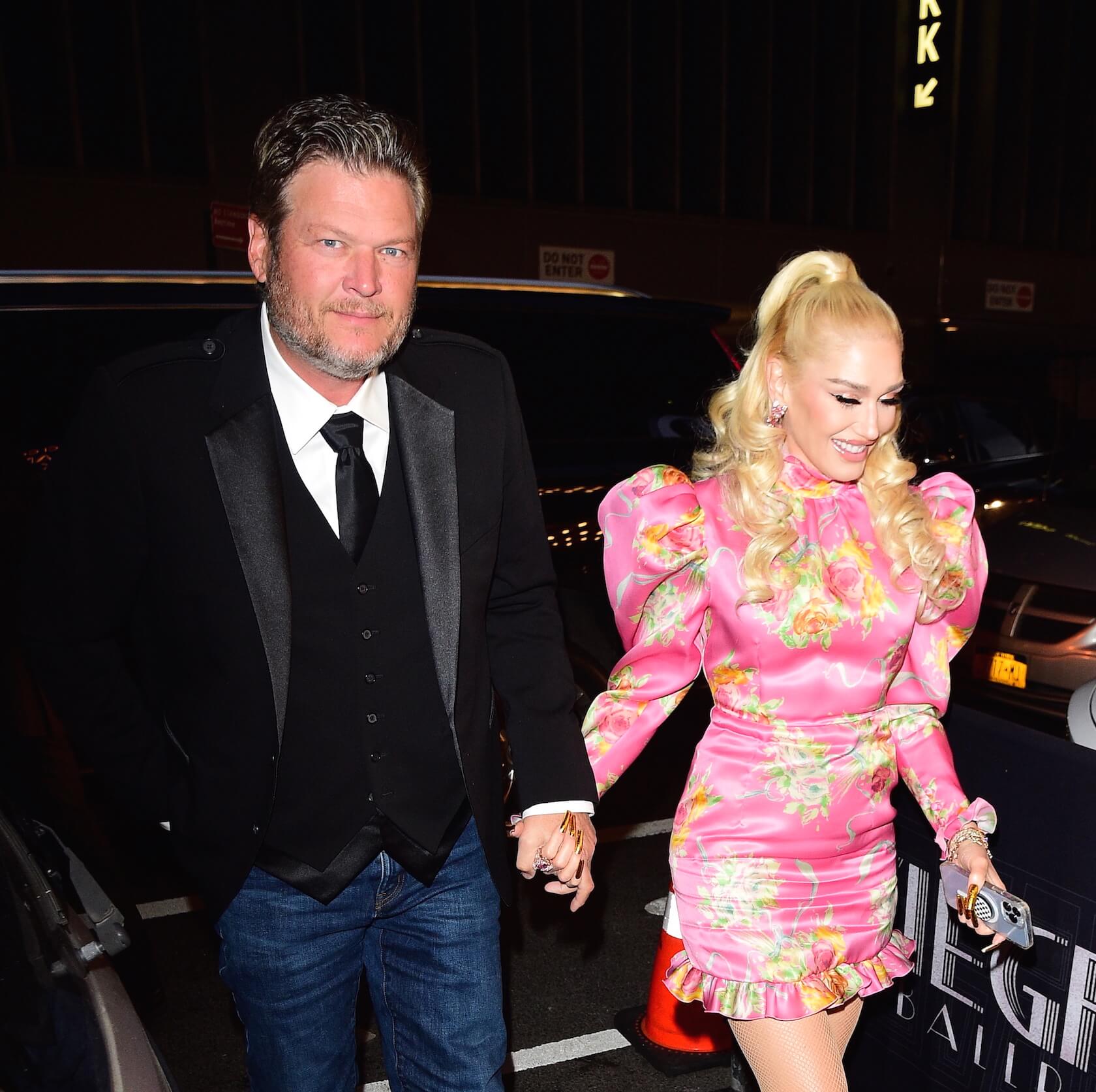 Blake Shelton in a suit holding hands and walking with 'The Voice' Season 24 coach Gwen Stefani in a pink dress