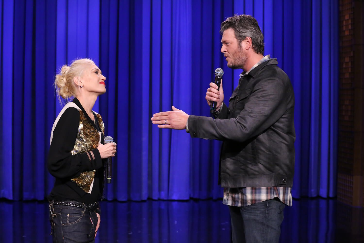 Gwen Stefani and Blake Shelton looking at each other with microphones in their hands on 'The Tonight Show Starring Jimmy Fallon'