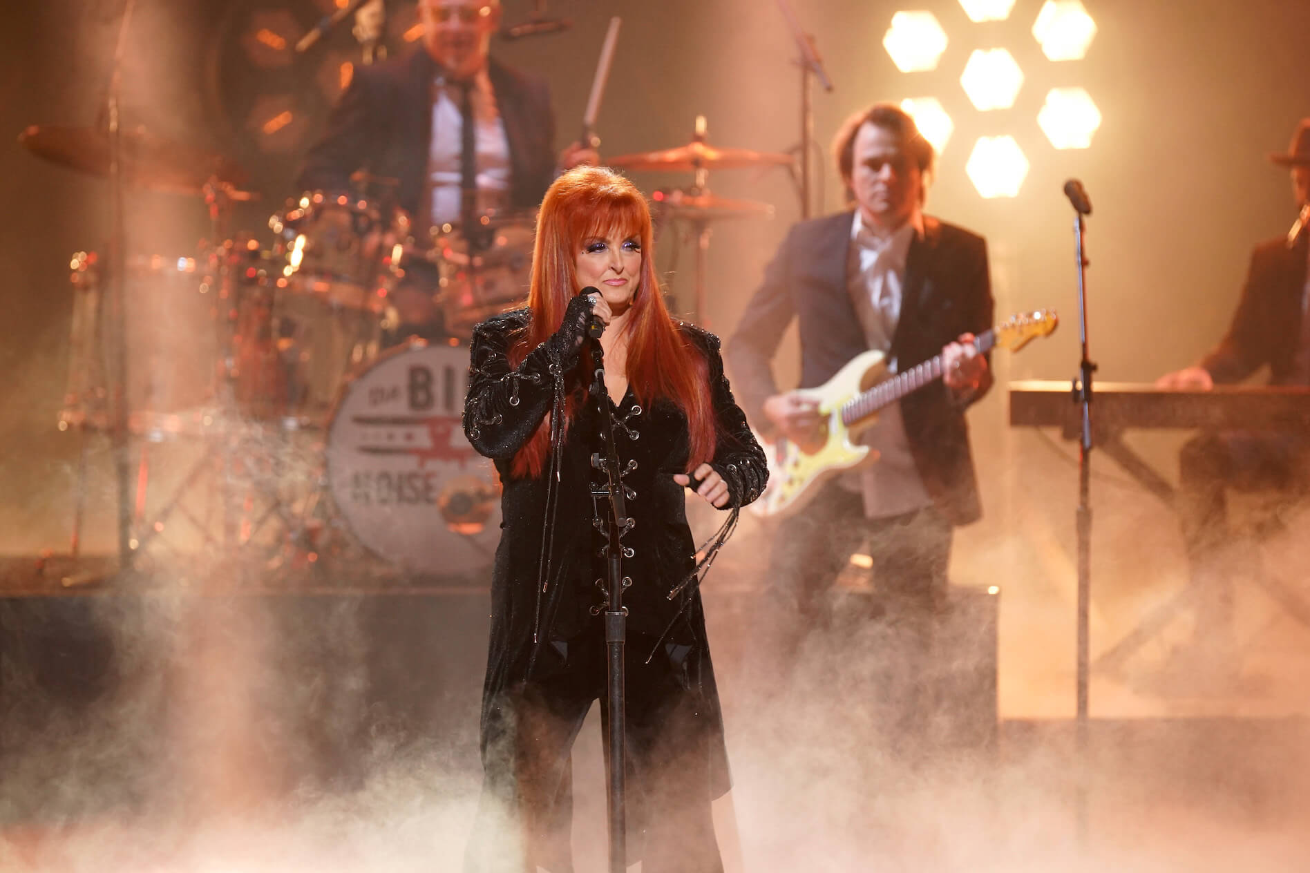 Wynonna Judd performing on stage ina cloud of fog with golden stage light behind her