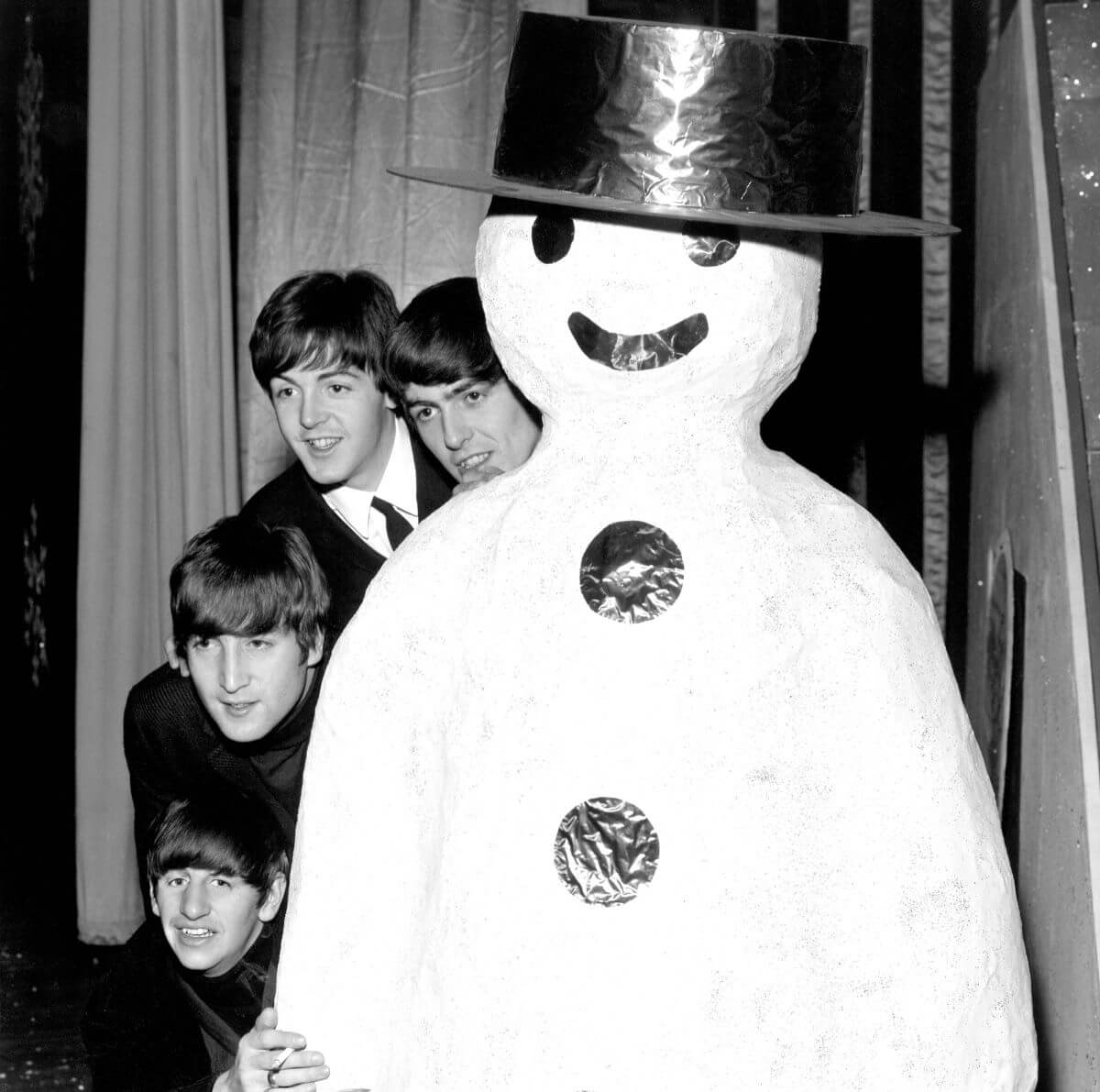 A black and white picture of The Beatles peeking out from the side of a large snowman statue.