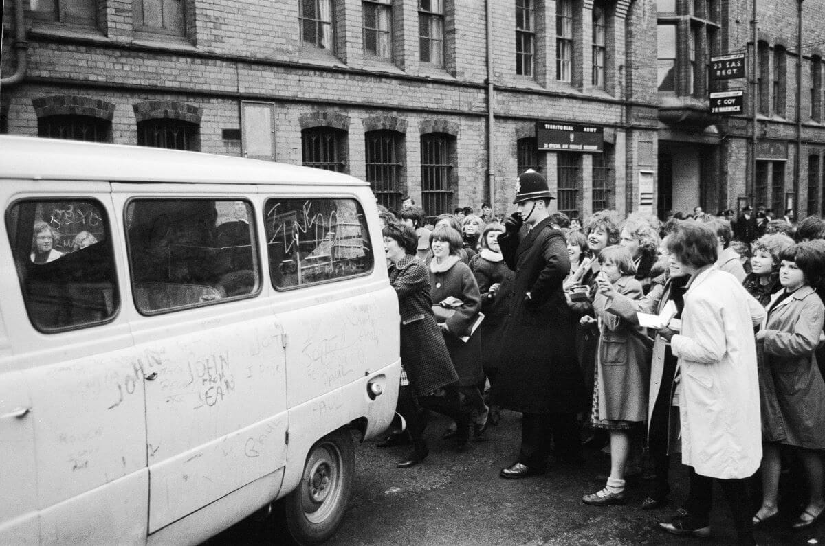 A crowd of fans follows behind The Beatles' van.