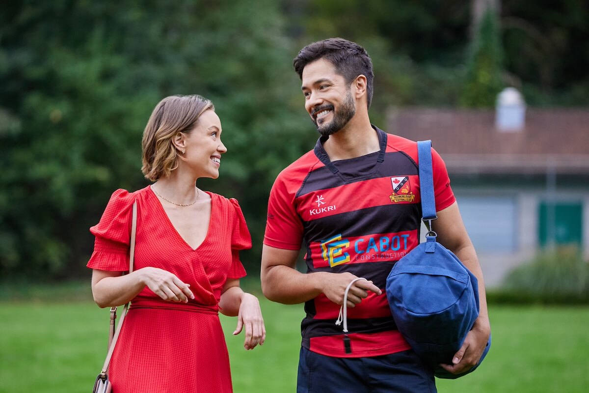 Laci J Mailey, in a red dress, standing next to Marco Grazzini, carrying a gym bag in the Hallmark movie 'Betty's Bad Luck in Love'