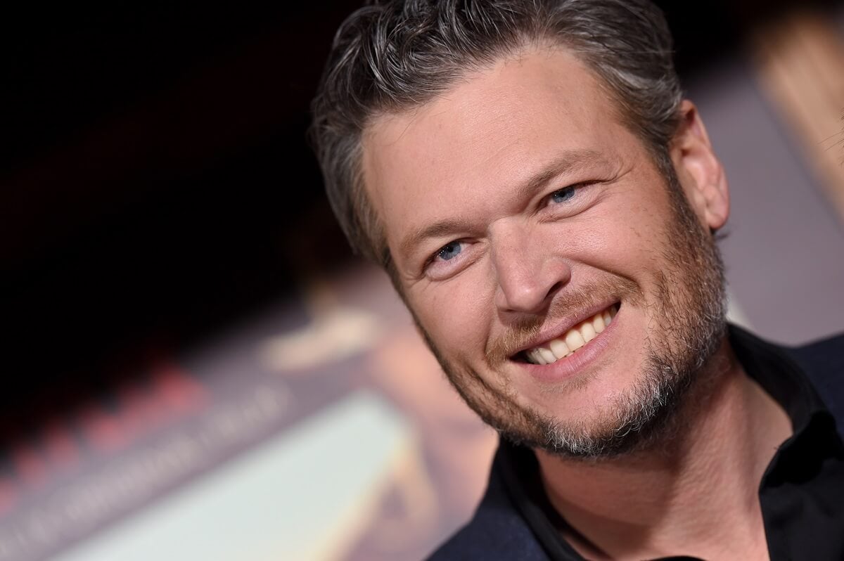 Blake Shelton smiling in a suit while arriving at the premiere of Netflix's at the premiere of Netflix's 'The Ridiculous 6'.
