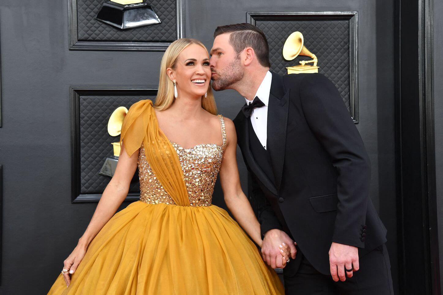 Carrie Underwood standing with her husband, Mike Fisher, kissing her cheek