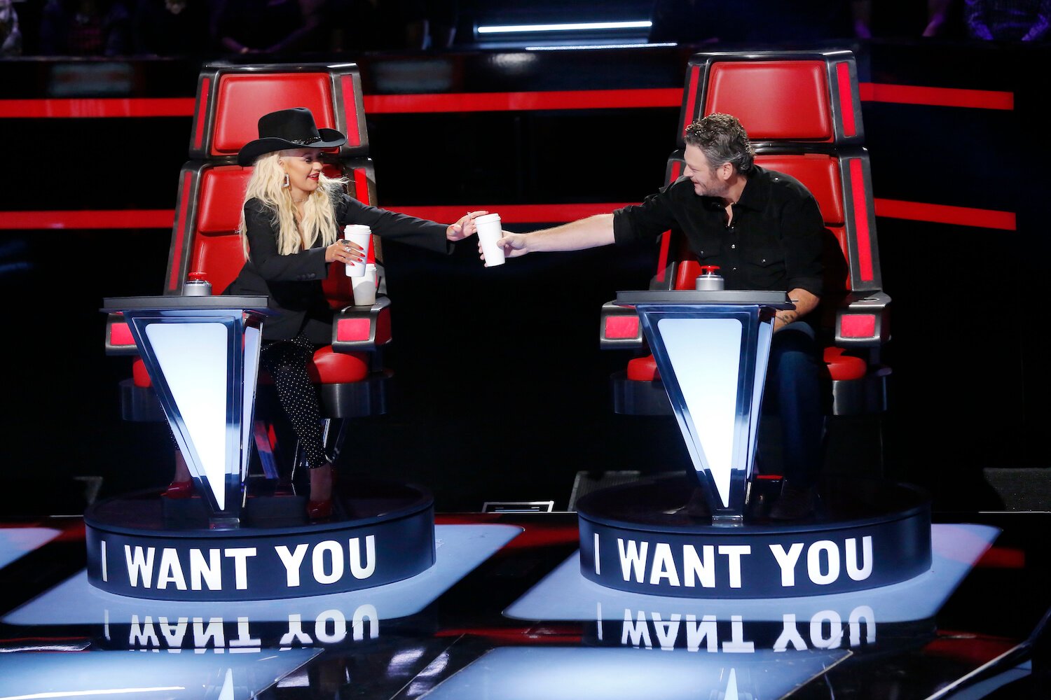 Christina Aguilera and Blake Shelton passing a drink in their coaching chairs on 'The Voice'