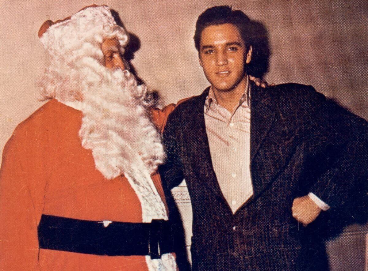 Elvis stands with his arm around Colonel Tom Parker, who wears a Santa suit.