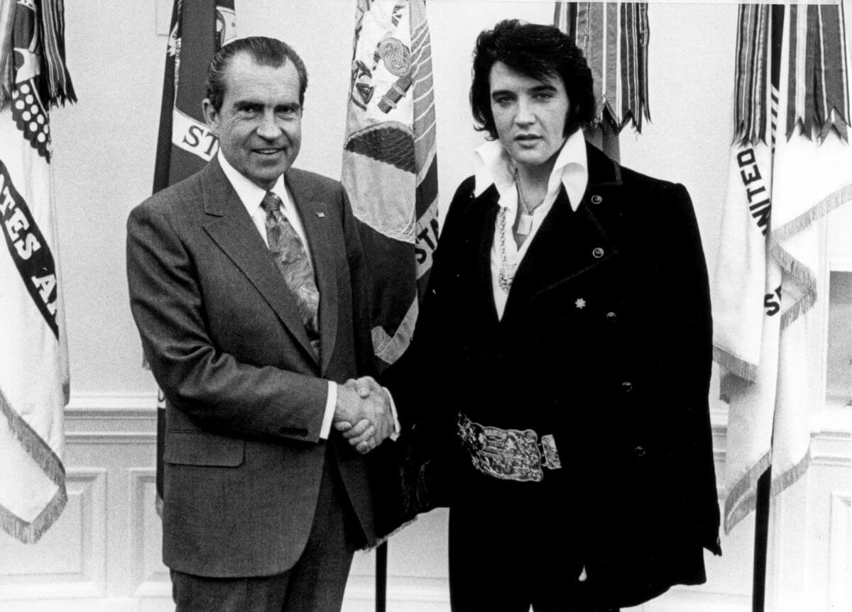 President Nixon and Elvis Presley shake hands in front of flags.