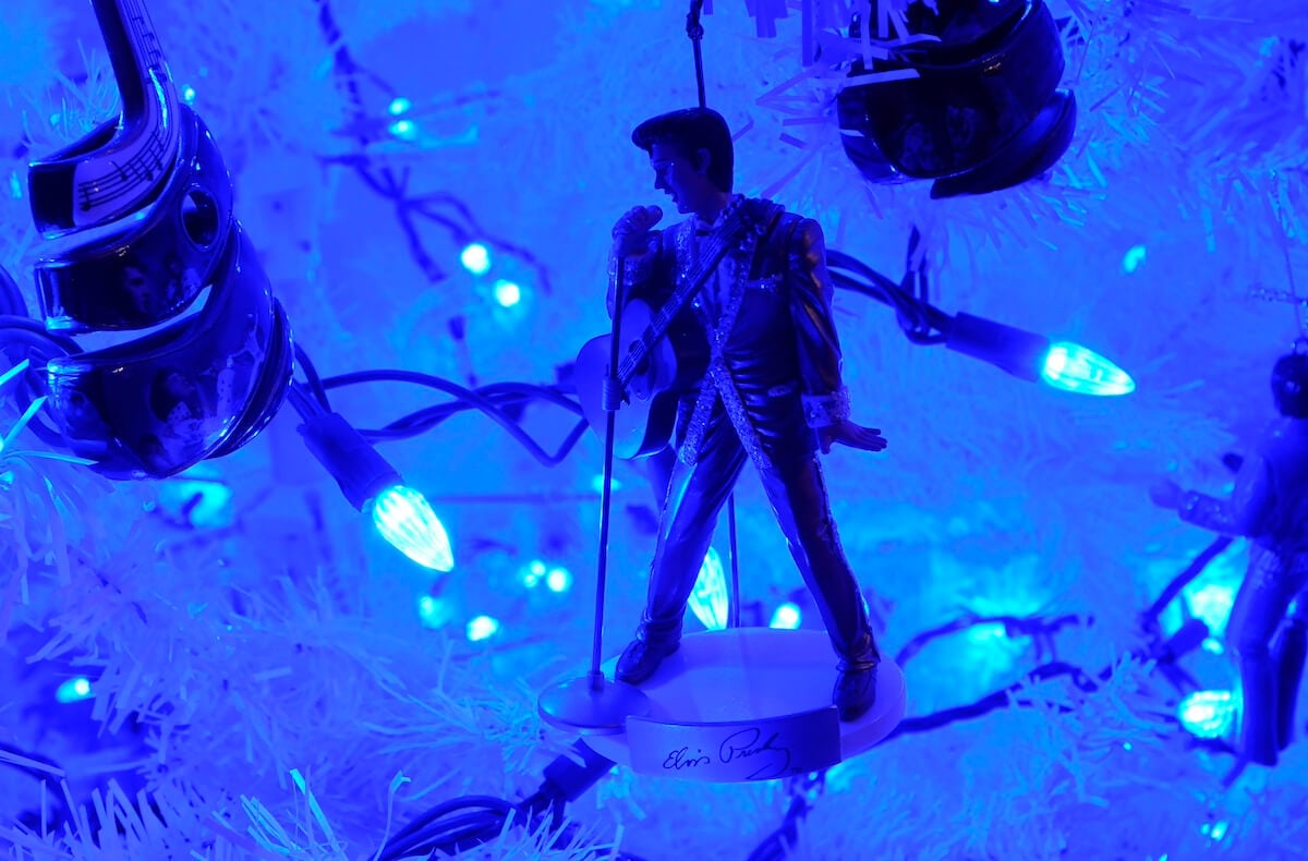 An Elvis Christmas ornament hanging on a white Christmas tree with blue lights