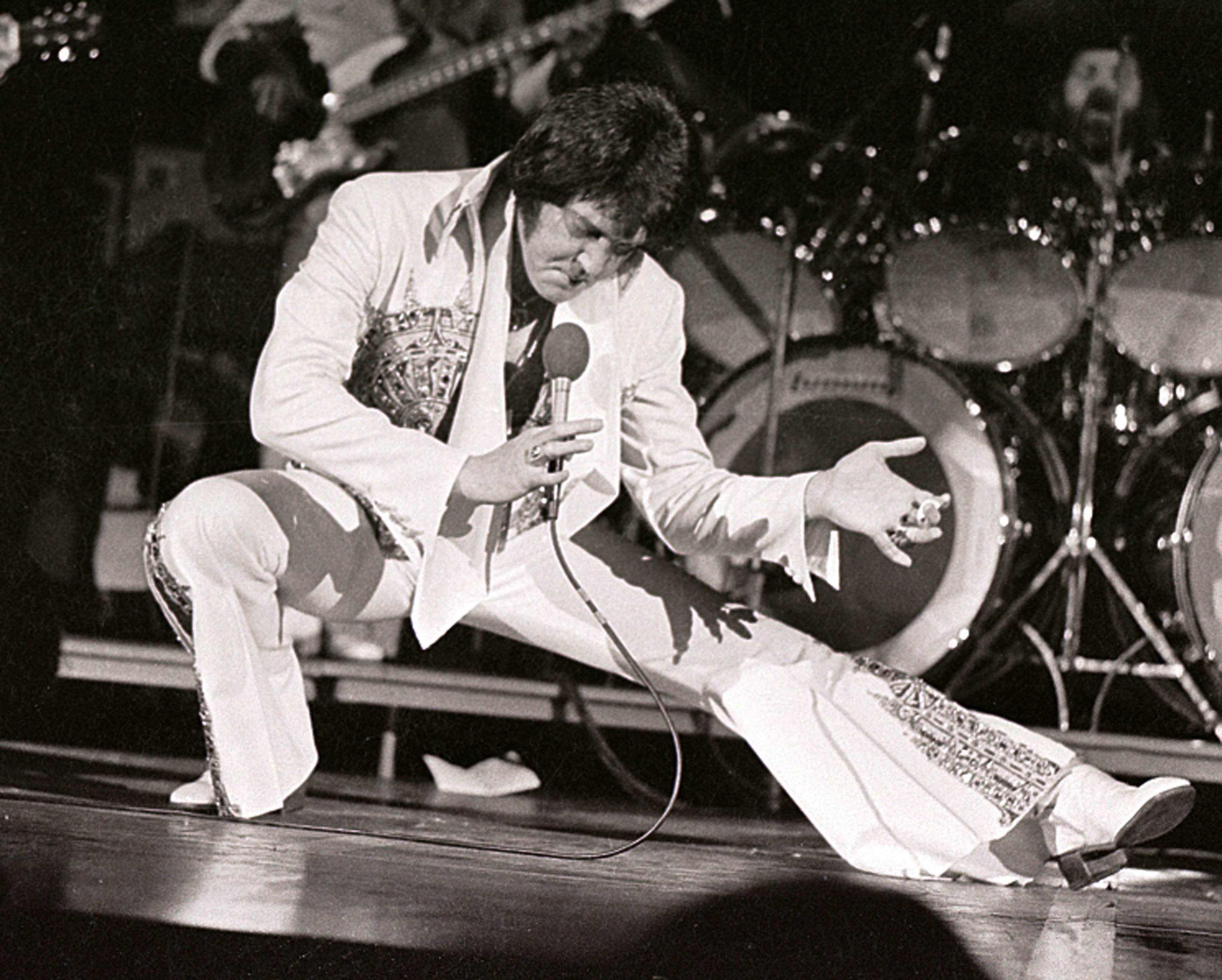 A black and white picture of Elvis Presley singing into a microphone while in a lunge position.