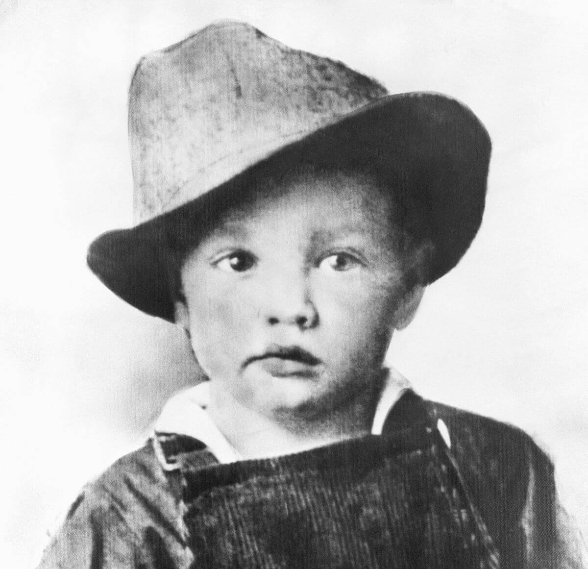 A black and white picture of a three-year-old Elvis Presley wearing a hat.