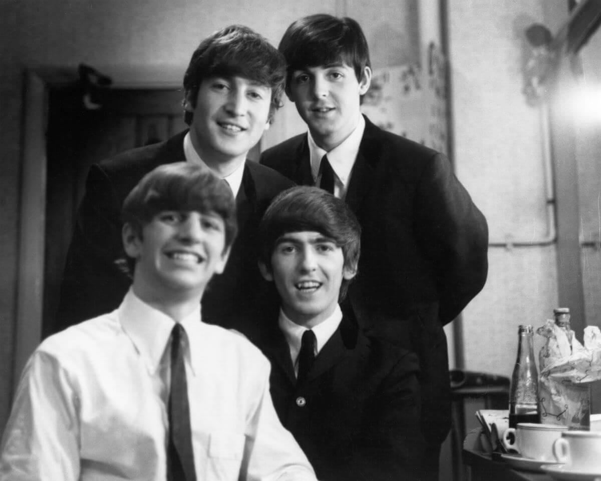 A black and white picture of John Lennon, Paul McCartney, Ringo Starr, and George Harrison of The Beatles. Starr and Harrison sit in front of Lennon and McCartney, who stand.