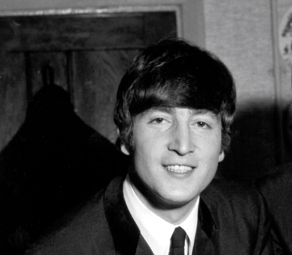 A black and white picture of John Lennon wearing a suit and smiling.