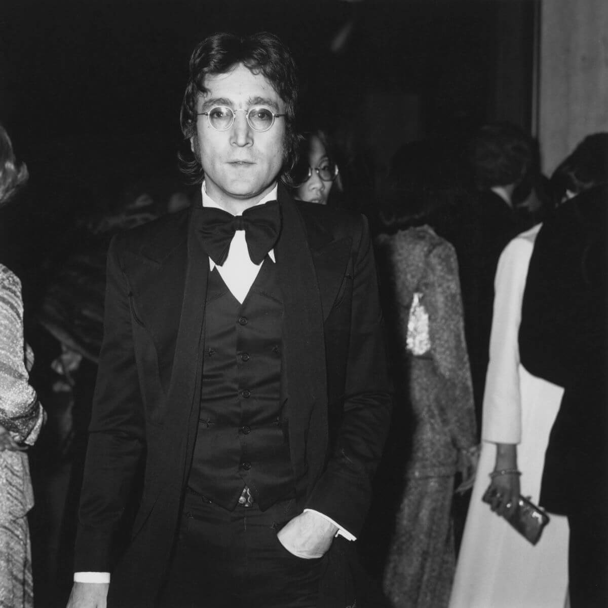 A black and white picture of John Lennon wearing glasses and a tuxedo.