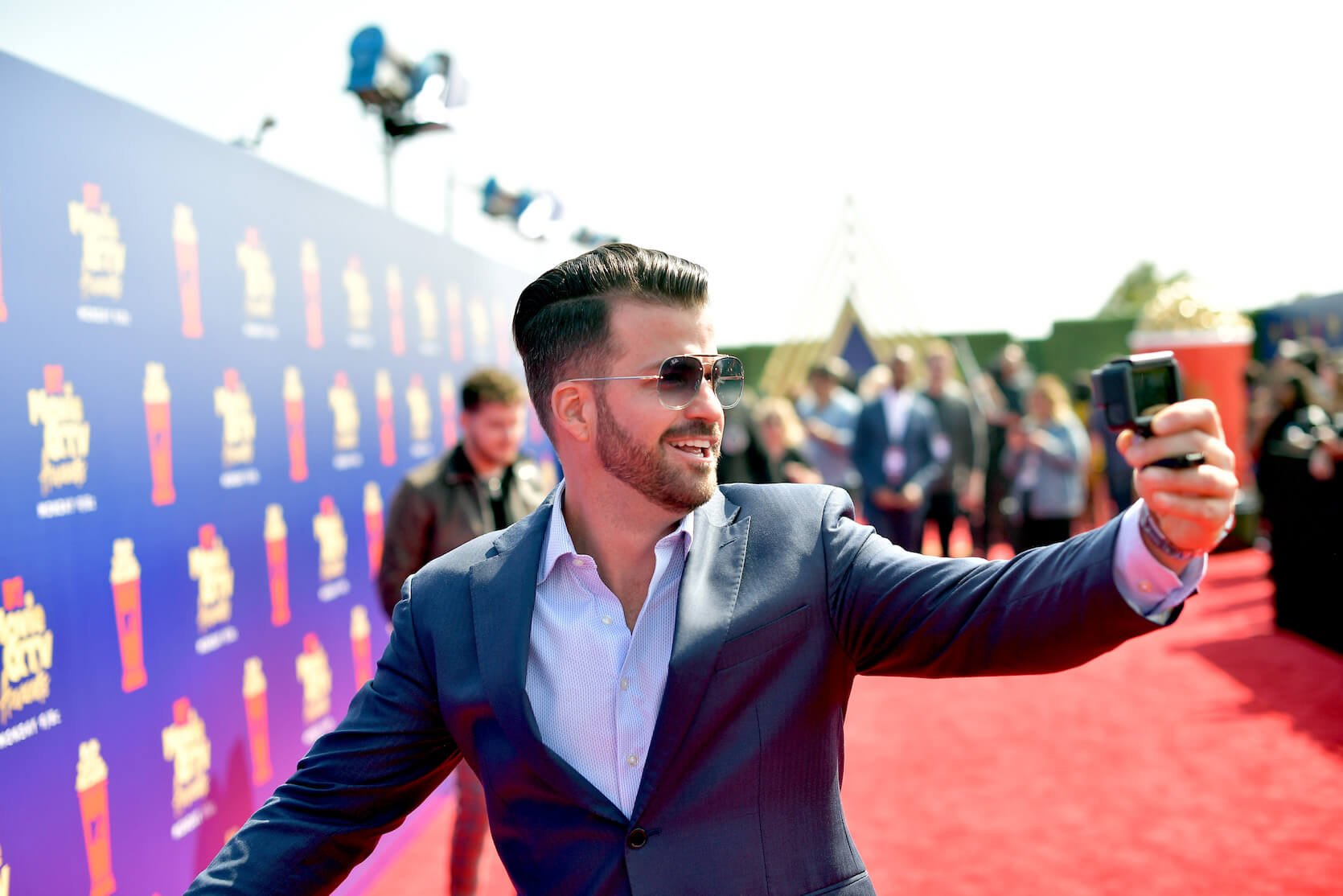 Johnny 'Bananas' Devenanzio from MTV's 'The Challenge' taking a selfie on the red carpet while wearing a suit and sunglasses.