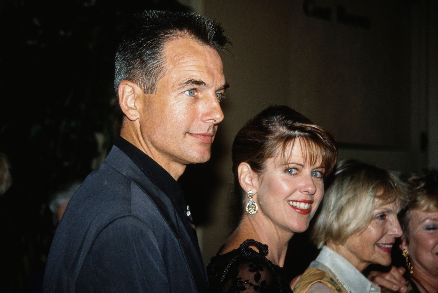 Mark Harmon and his wife, Pam Dawber, standing next to each other at an event. Dawber is looking over her shoulder at the camera. 