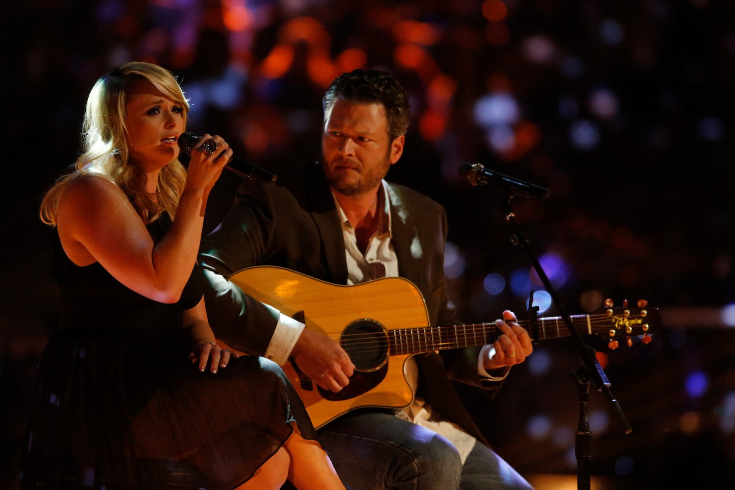 Miranda Lambert singing next to Blake Shelton playing guitar in dim lighting