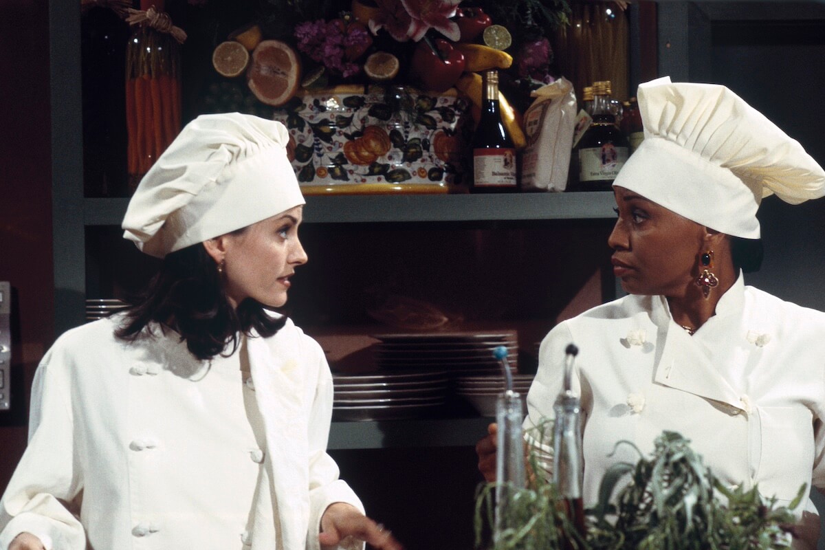 Monica (Courteney Cox) in a chef's uniform talking to another chef in 'Friends' Season 1