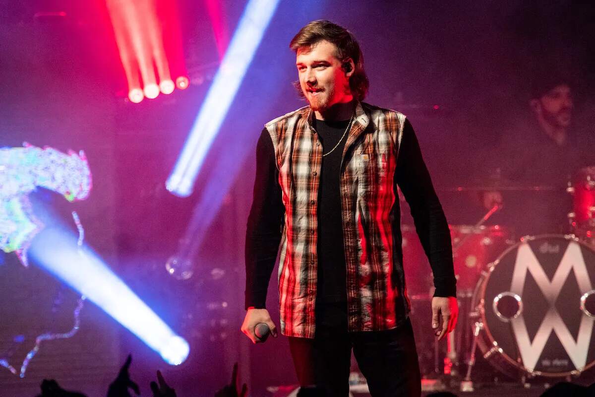Country star Morgan Wallen looks at the crowd while holding a microphone and wearing a plaid shirt