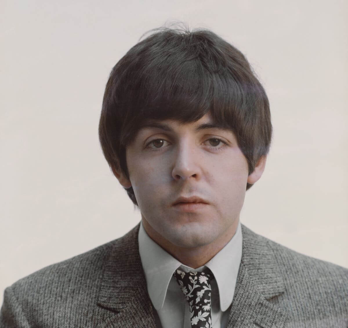 Paul McCartney wears a gray suit with a black and white floral tie.