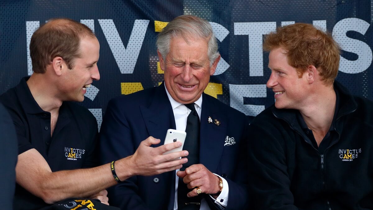 ce William and Prince Harry with King Charles laughing at something they're showing him on an iPhone