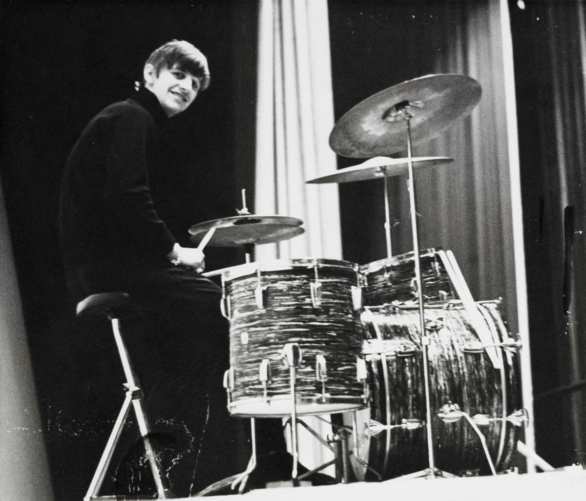 A black and white picture of Ringo Starr sitting a drum set. 