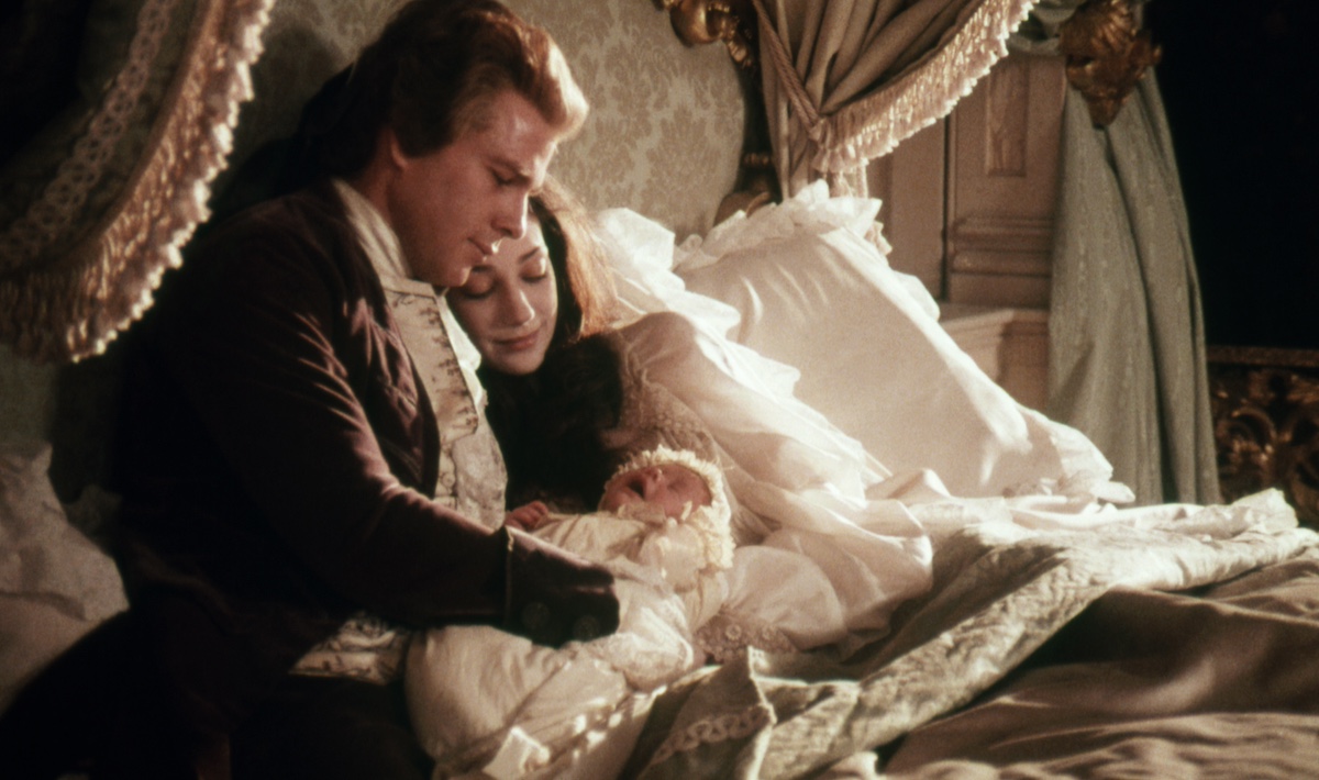Ryan O'Neal sitting on a bed next to Marisa Berenson in 18th century costumes in 'Barry Lyndon'
