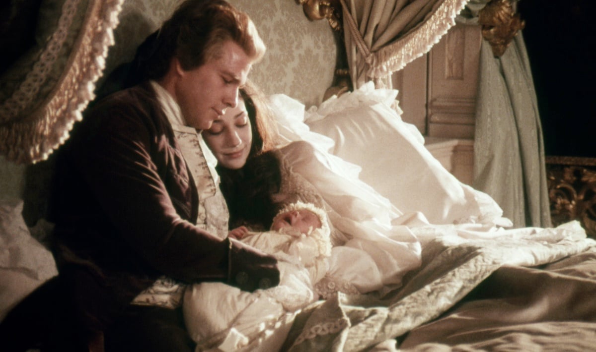 Ryan O'Neal sitting on a bed next to Marisa Berenson in 18th century costumes in 'Barry Lyndon'