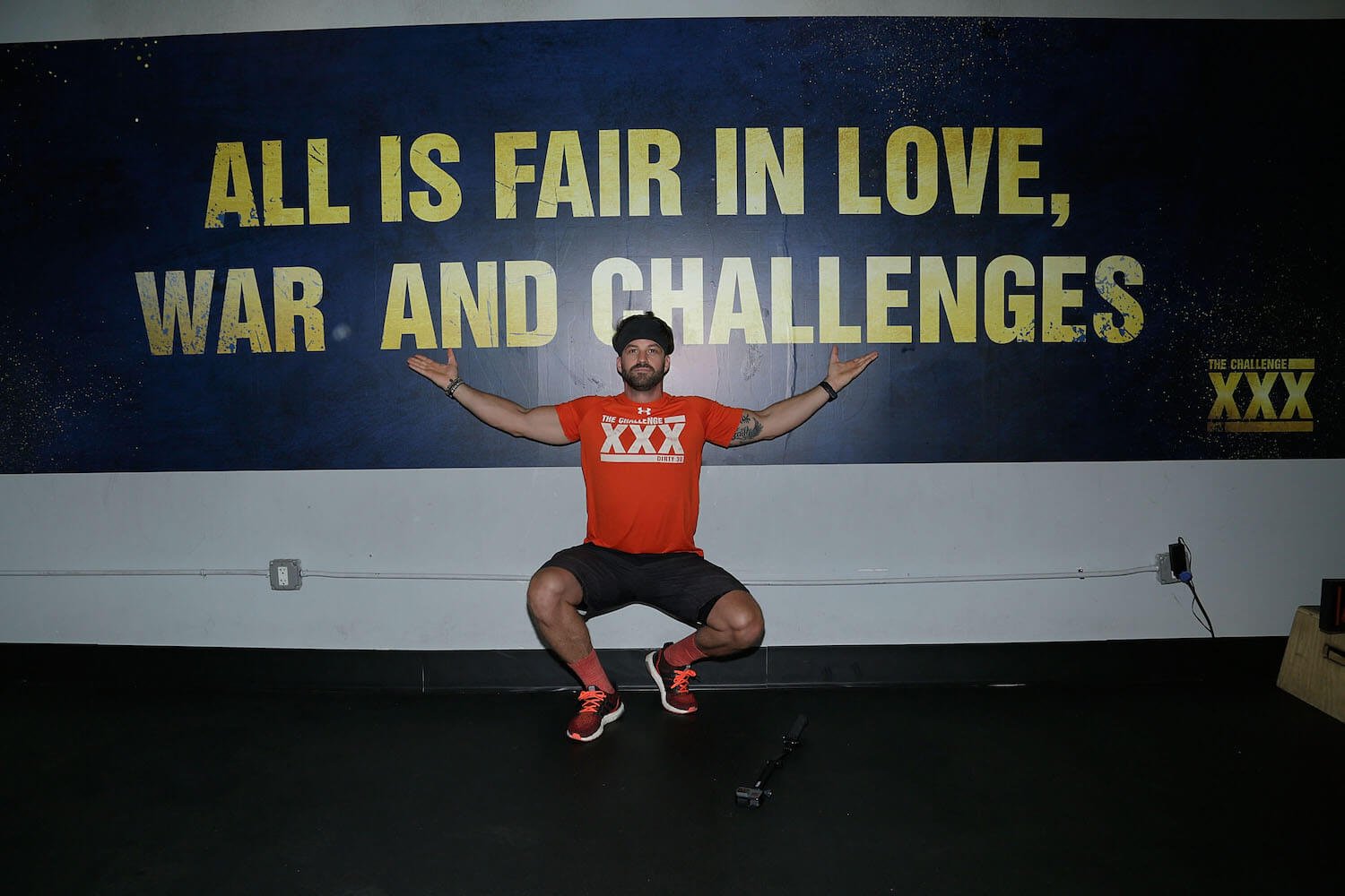 Johnny 'Bananas' Devenanzio from MTV's 'The Challenge' posing in front of a sign that says "All is fair in love, war, and challenges'