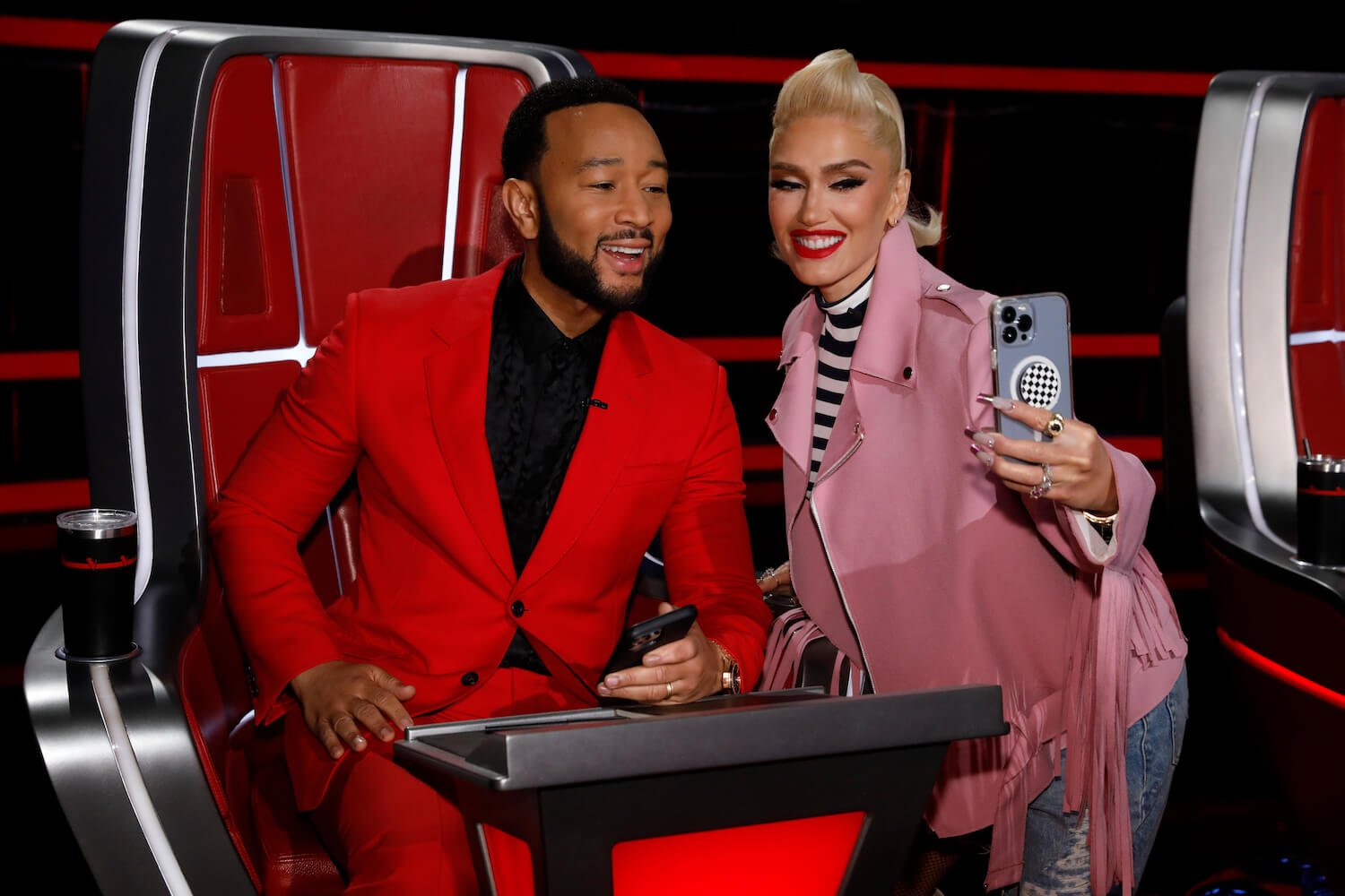 'The Voice' Season 24 coaches John Legend and Gwen Stefani smiling next to each other while Stefani holds her phone for a selfie
