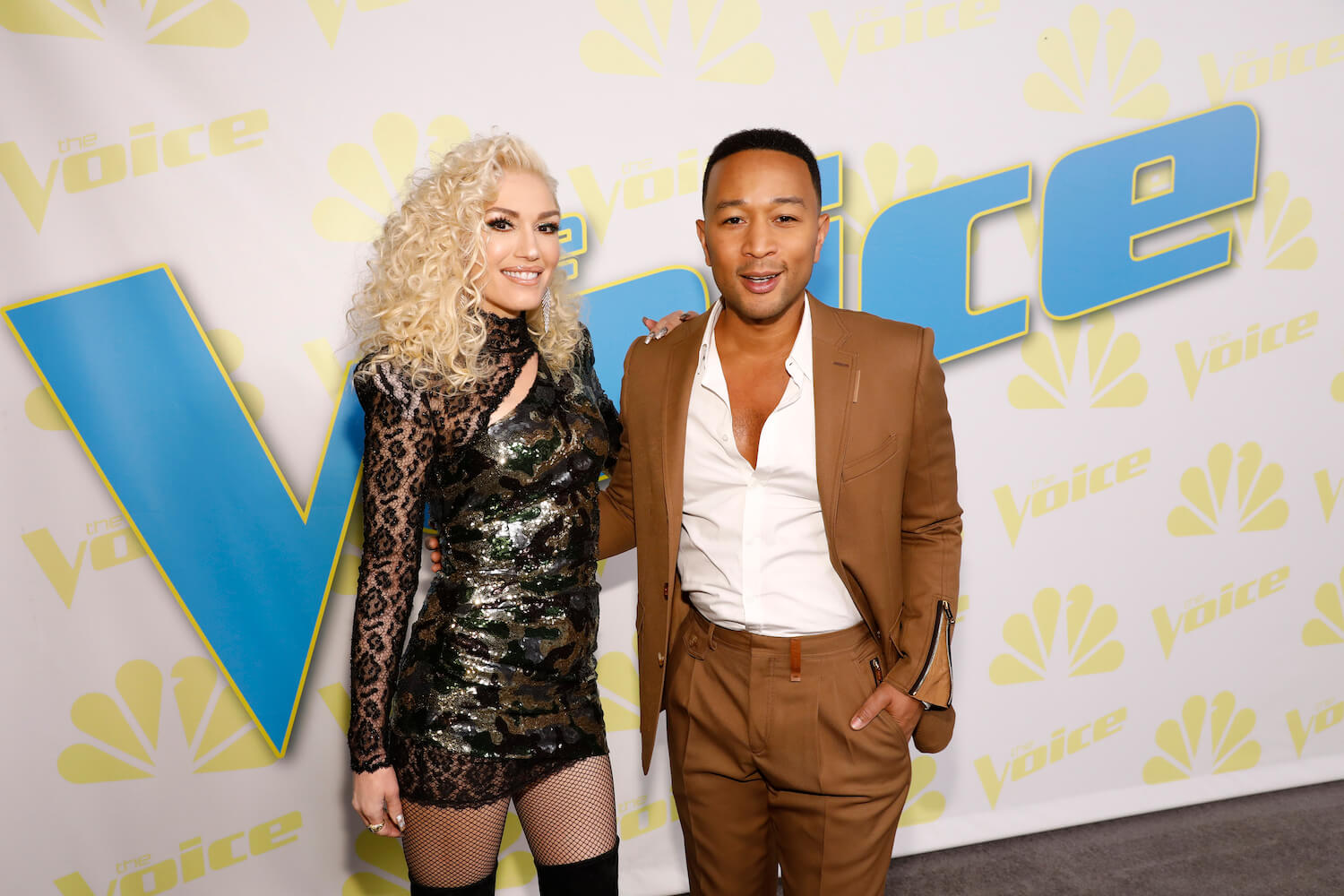 'The Voice' Season 24 coaches Gwen Stefani and John Legend smiling while standing next to each other in front of 'The Voice' sign