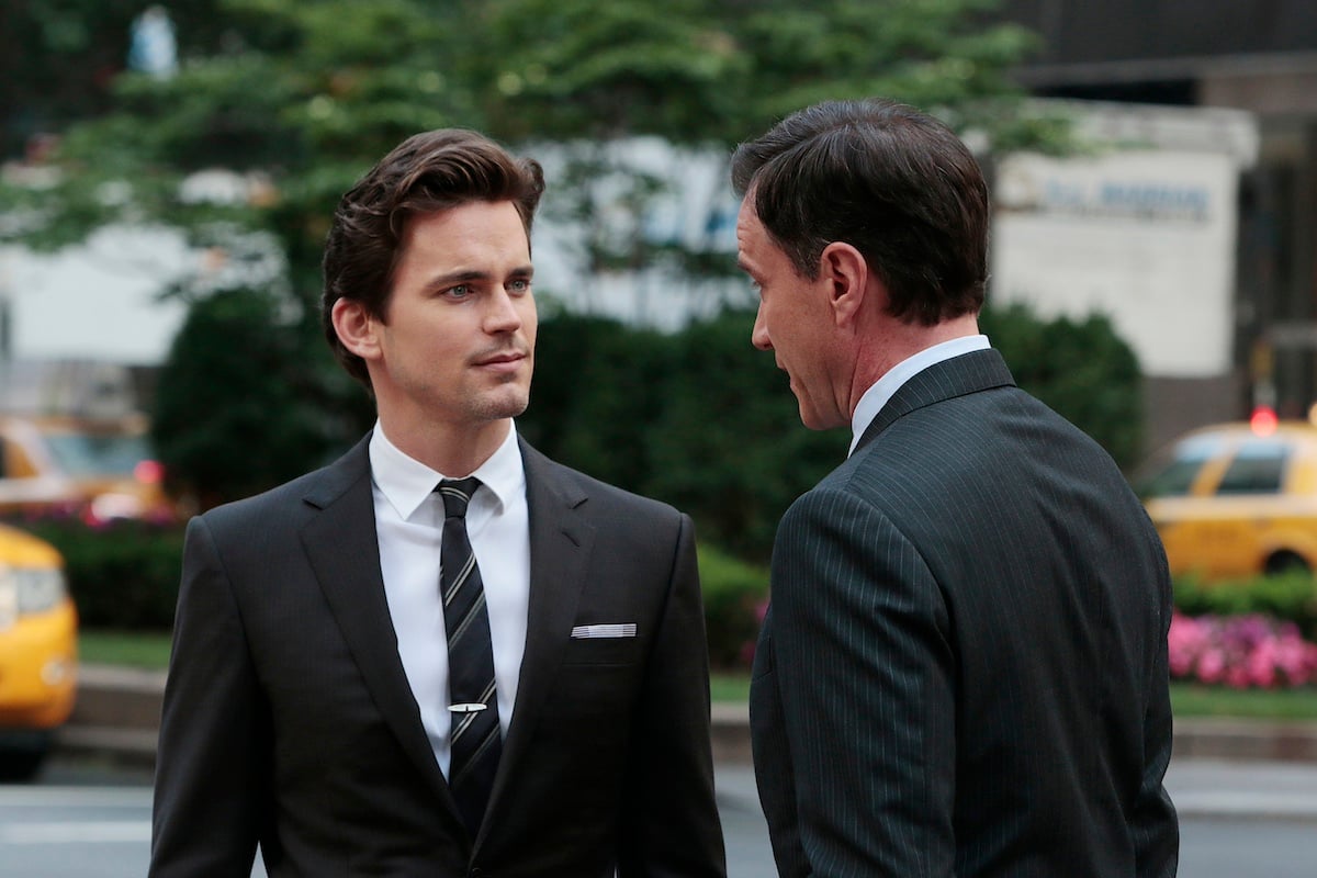 Matt Bomer, in a black suit, talking to a man in 'White Collar'