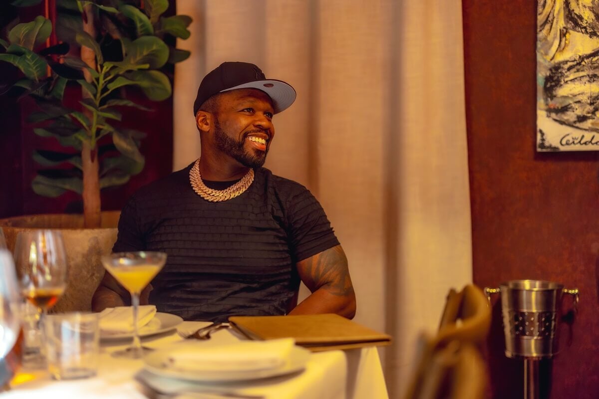50 Cent posing in a black shirt while sitting at a table.