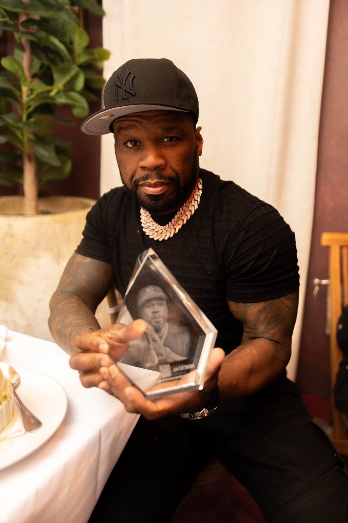 50 Cent sitting in a chair posing in a chair holding a glass object.