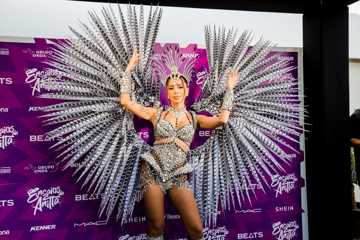 Anitta stands in front of a purple step and repeat wearing a rhinstoned costume.