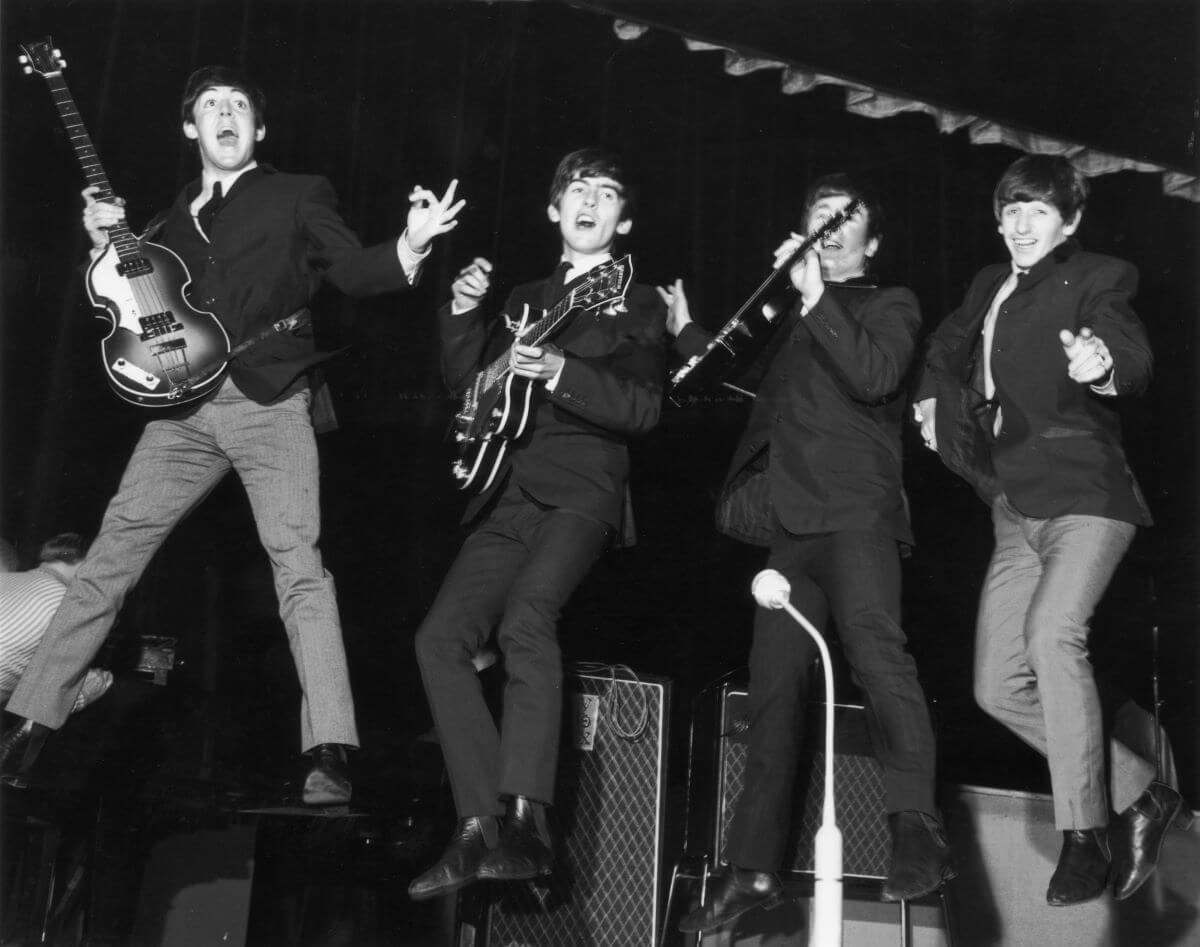 A black and white picture of Paul McCartney, George Harrison, John Lennon, and Ringo Starr of The Beatles jumping in the air. McCartney, Harrison, and Lennon hold guitars.