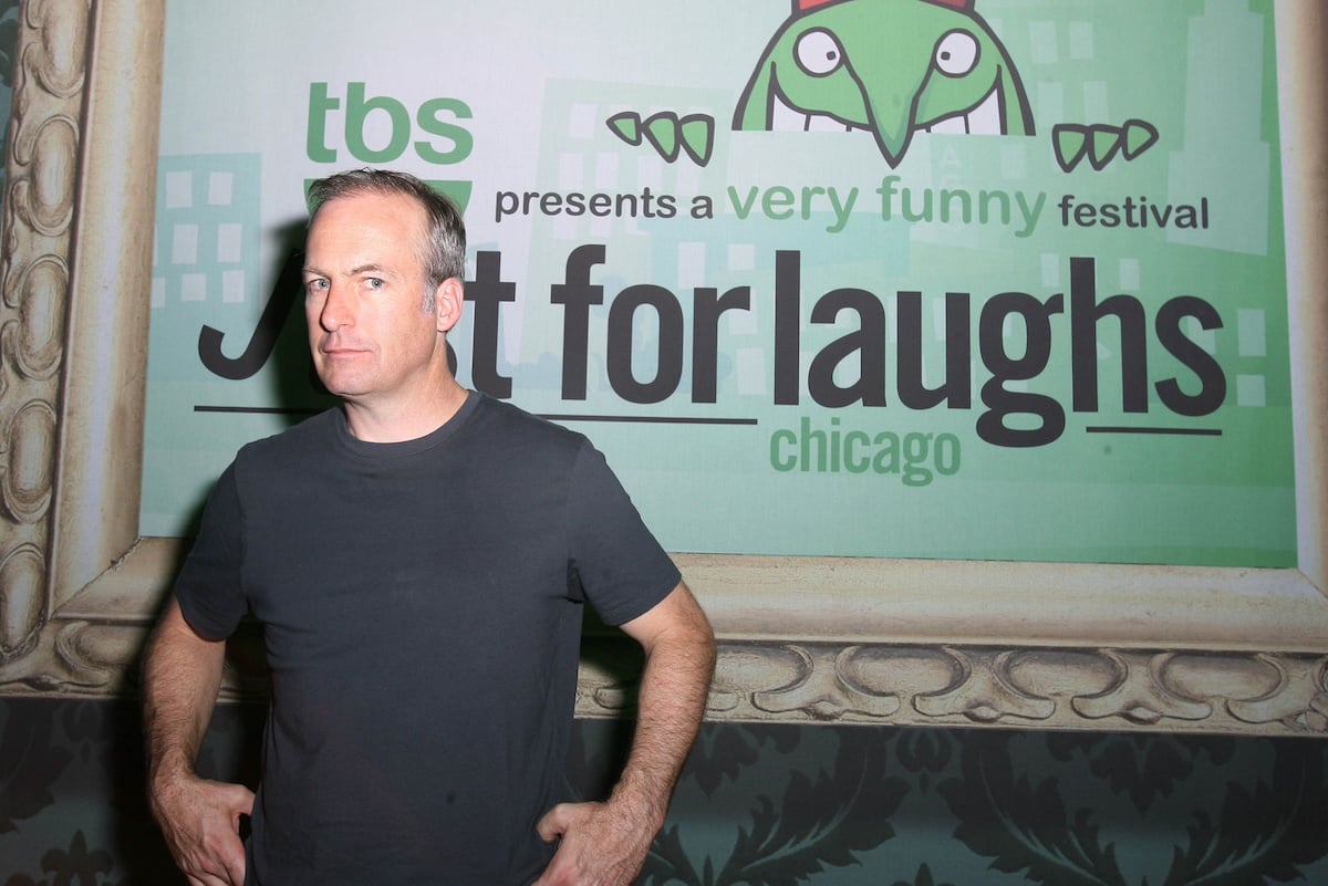 Bob Odenkirk in a T-shirt standing in front of a poster advertising the Just for Laughs comedy festival