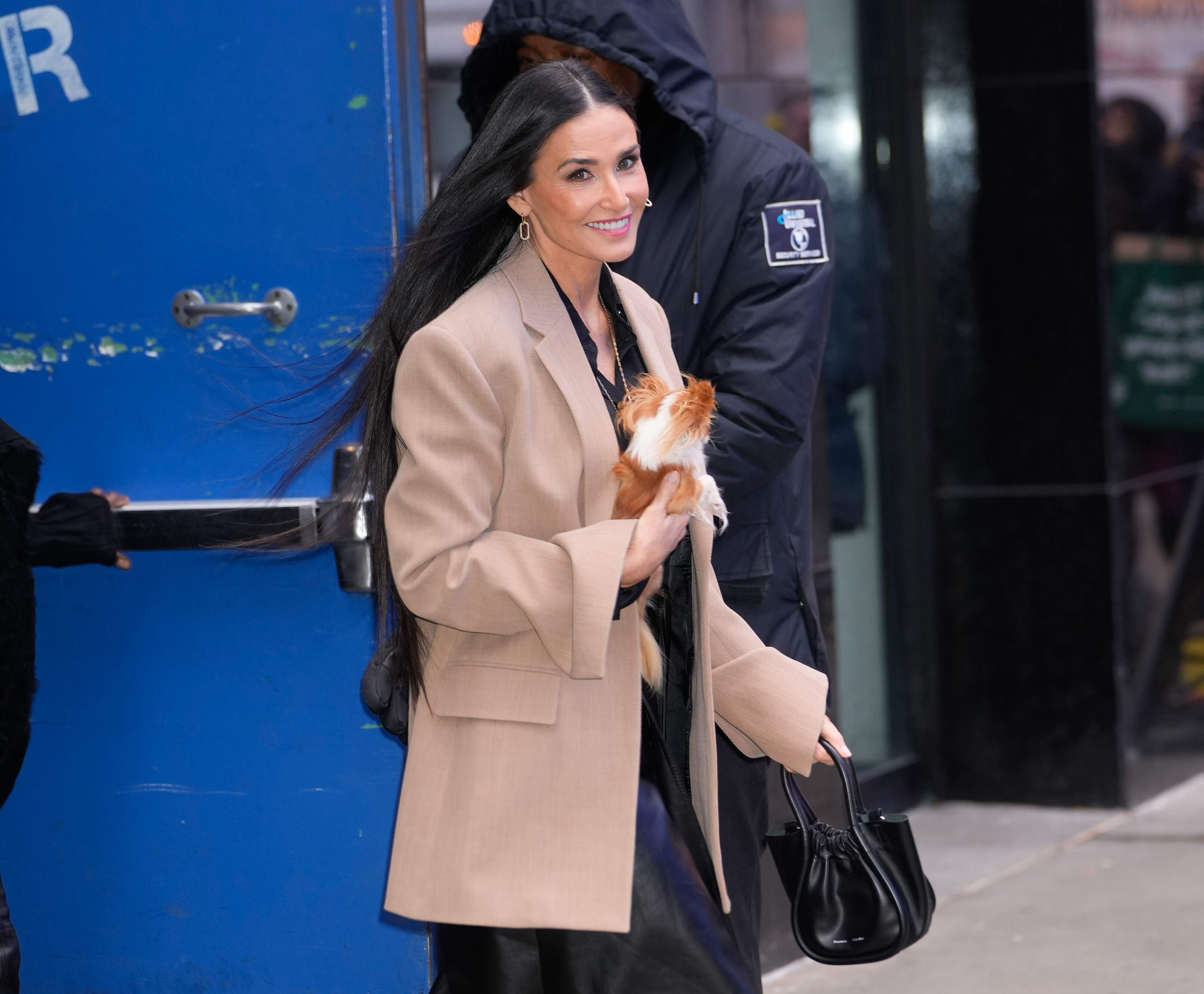 Actor Demi Moore walks with her chihuahua across a street in NYC while wearing a tan blazer and white boots