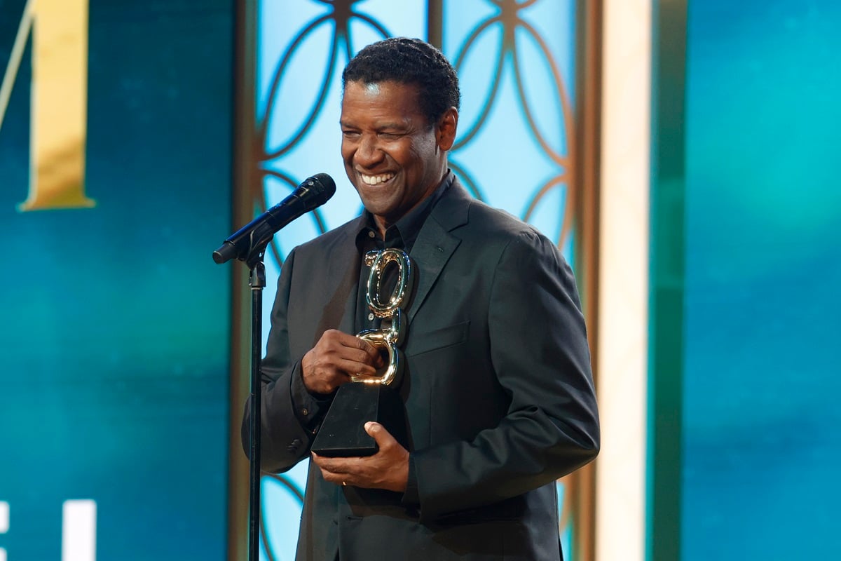 Denzel Washington accepting the Film Icon award on stage in a green suit.