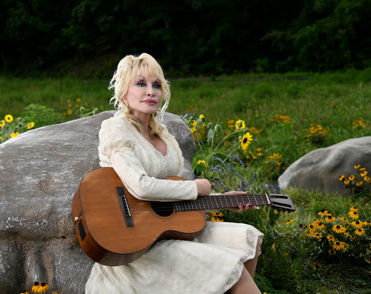 Dolly Parton holding a guitar while playing herself in the musical comedy Dolly Parton's Mountain Magic Christmas.