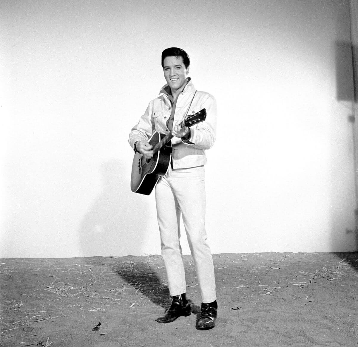 A black and white picture of Elvis Presley standing with an acoustic guitar.