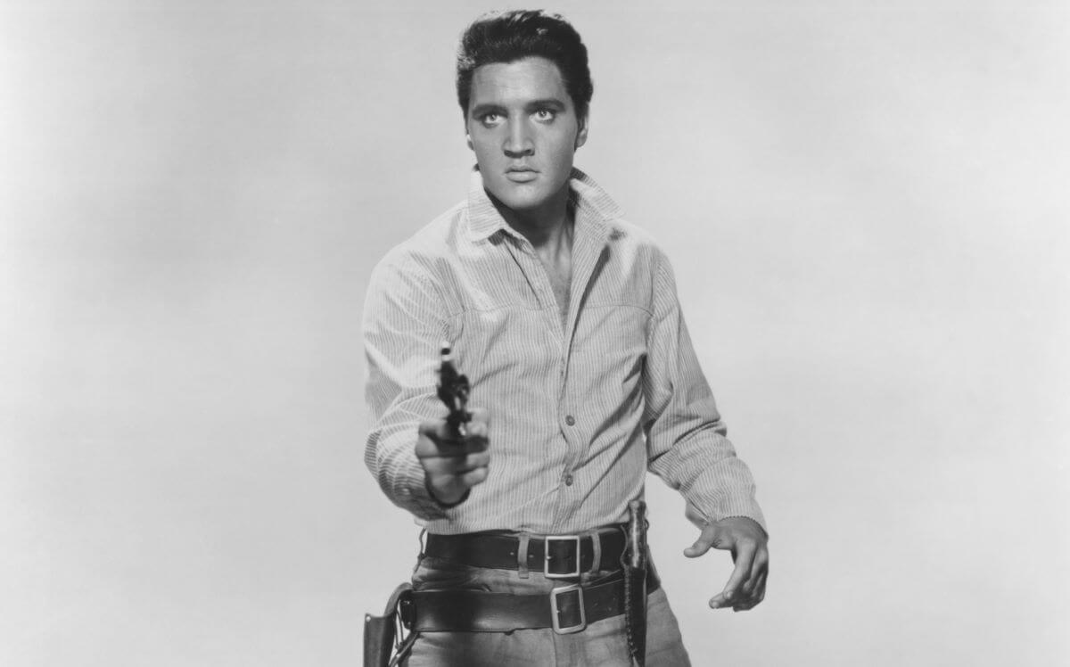 A black and white picture of Elvis pointing a gun at the camera.