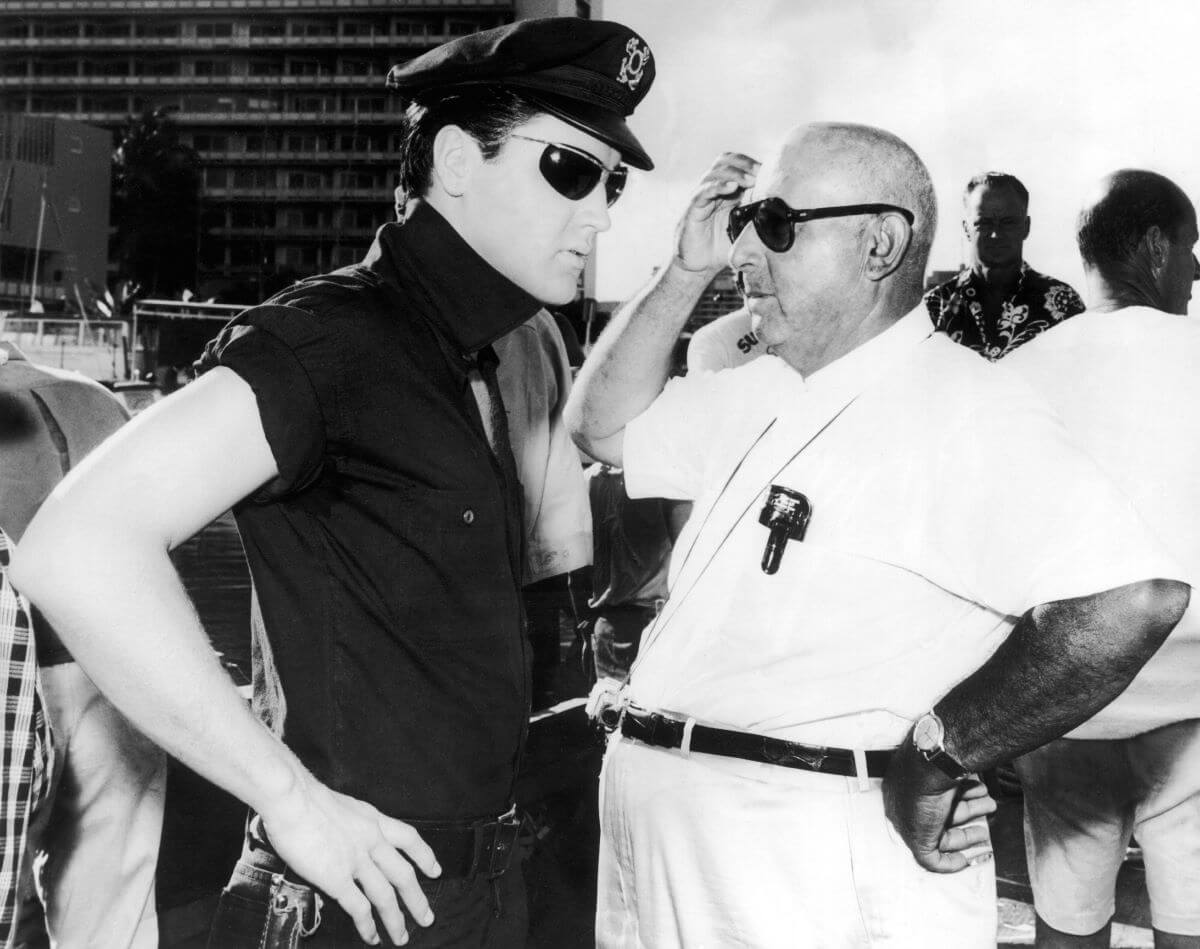 A black and white picture of Elvis Presley wearing a police uniform and standing next to director Norman Taurog.