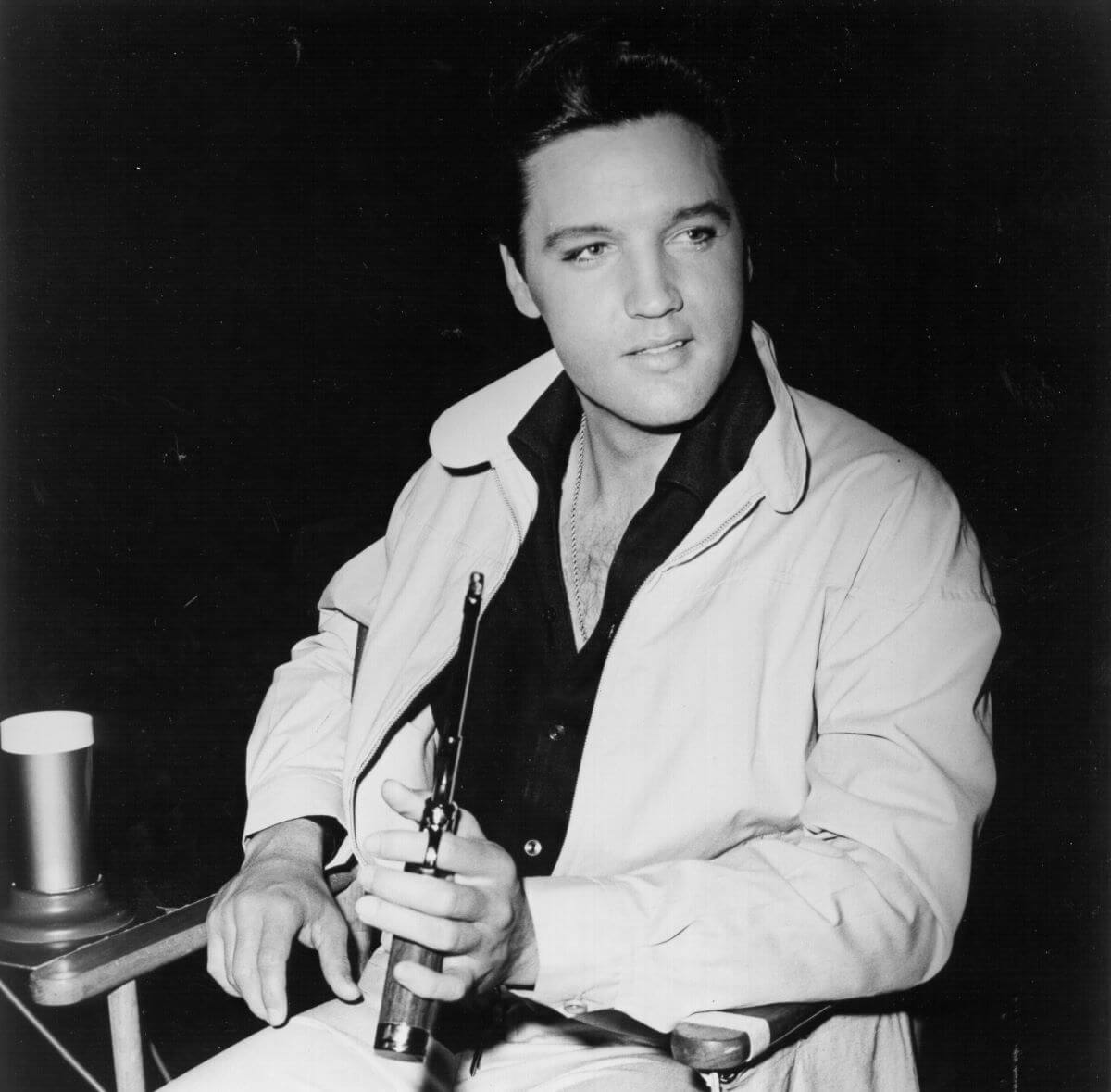 A black and white picture of Elvis sitting and holding a gun.