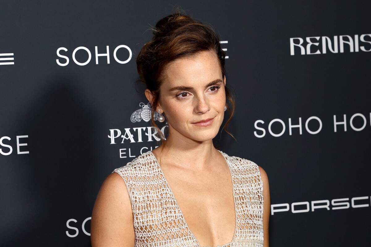 Actor Emma Watson wears a netted dress with her hair up and smiles on the red carpet in 2023
