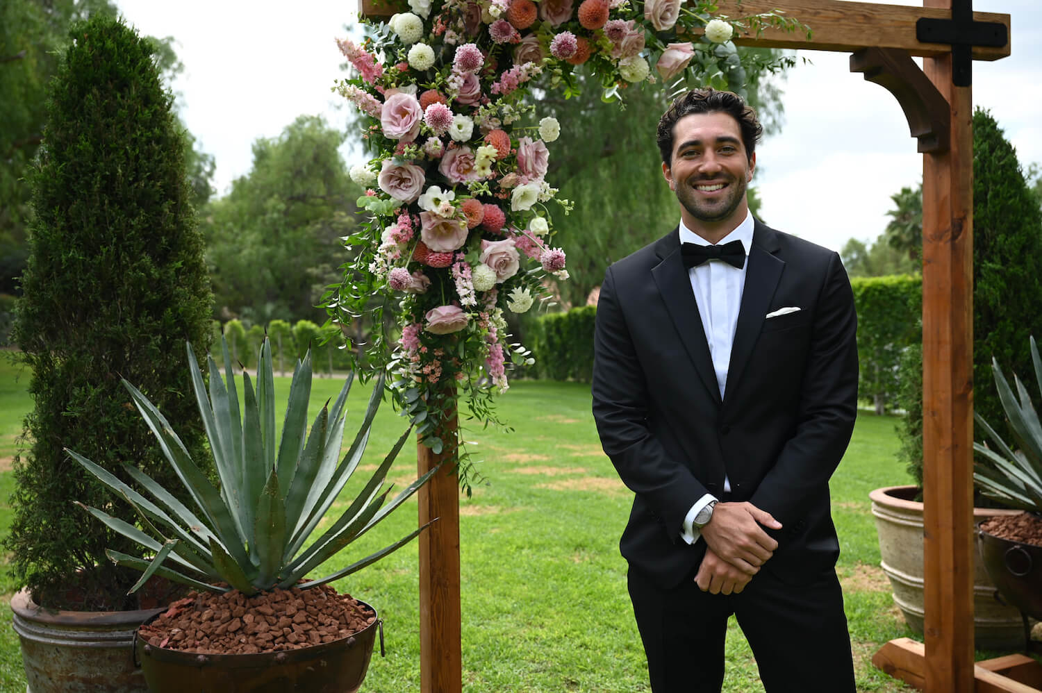 'The Bachelor' Season 28 star Joey Graziadei smiling in a tux while standing in front of a flower arch