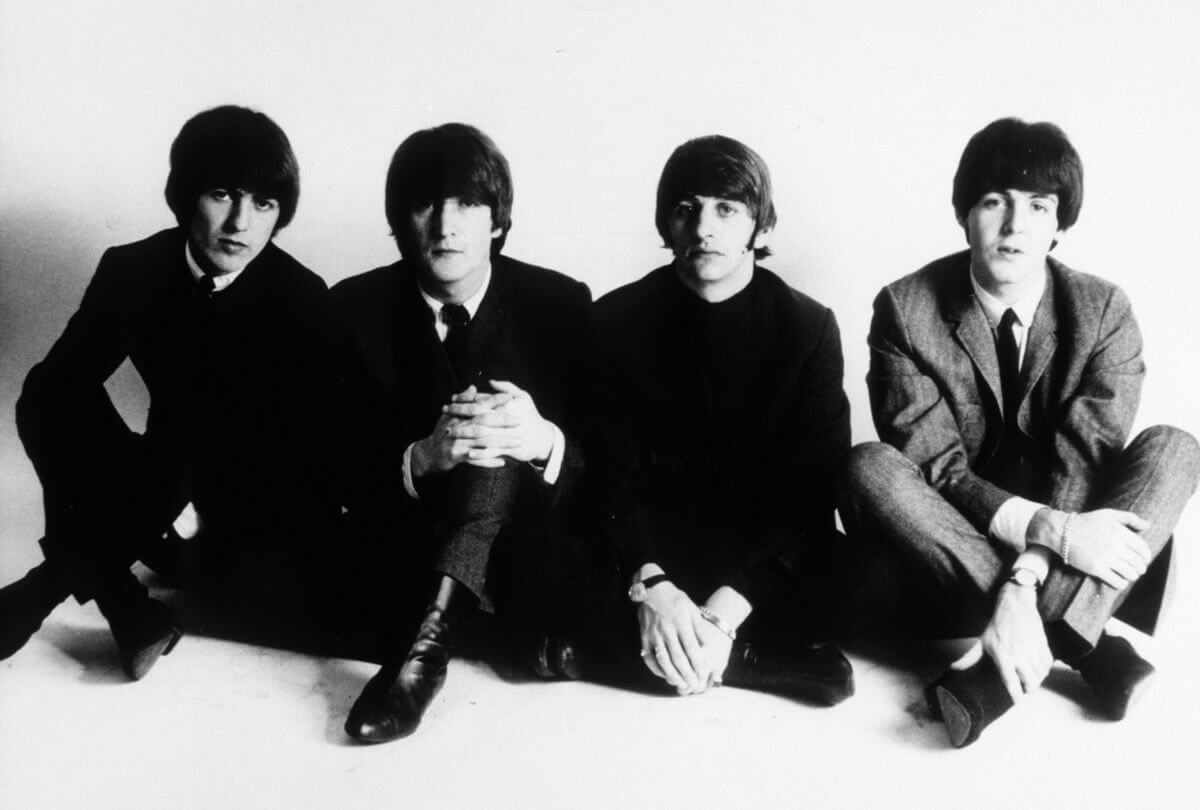 A black and white picture of George Harrison, John Lennon, Ringo Starr, and Paul McCartney sitting on the floor.